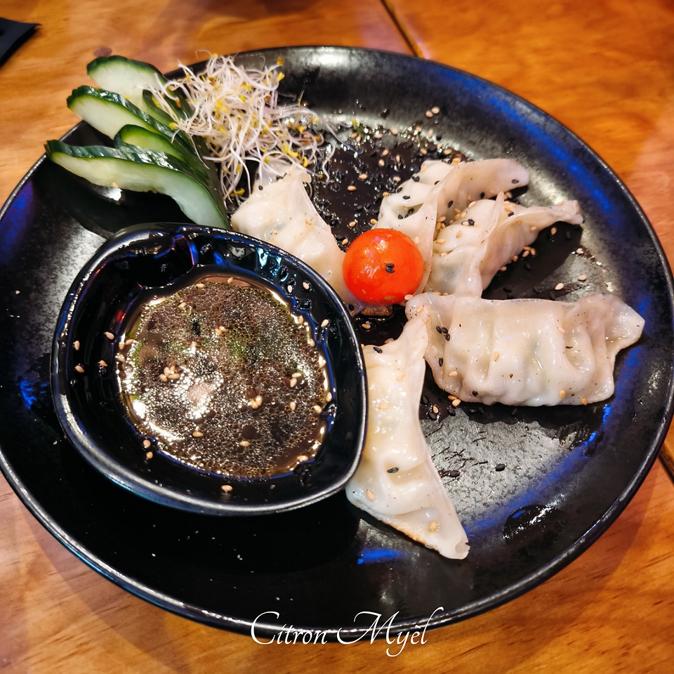 Assiette de Gyozas poulet et légumes accompagnée d'une sauce, concombre et tomate cerise