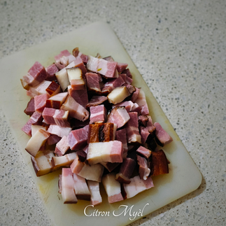 lard fumé découpé en morceaux sur une planche à découpée blanche.
