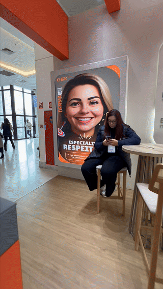 Visitante interage com totem Phygital no stand da GSK durante o TERADERM 2025, gerando avatar por IA e tendo sua imagem exibida na Social Wall em tempo real.