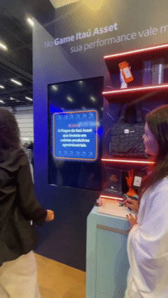 Participante interage com totem touchs Phygital Solutions em jogo de memória educativo do Itaú no XP Expert. A ativação premia de acordo com o desempenho e exibe conteúdos explicativos sobre investimentos durante a partida.