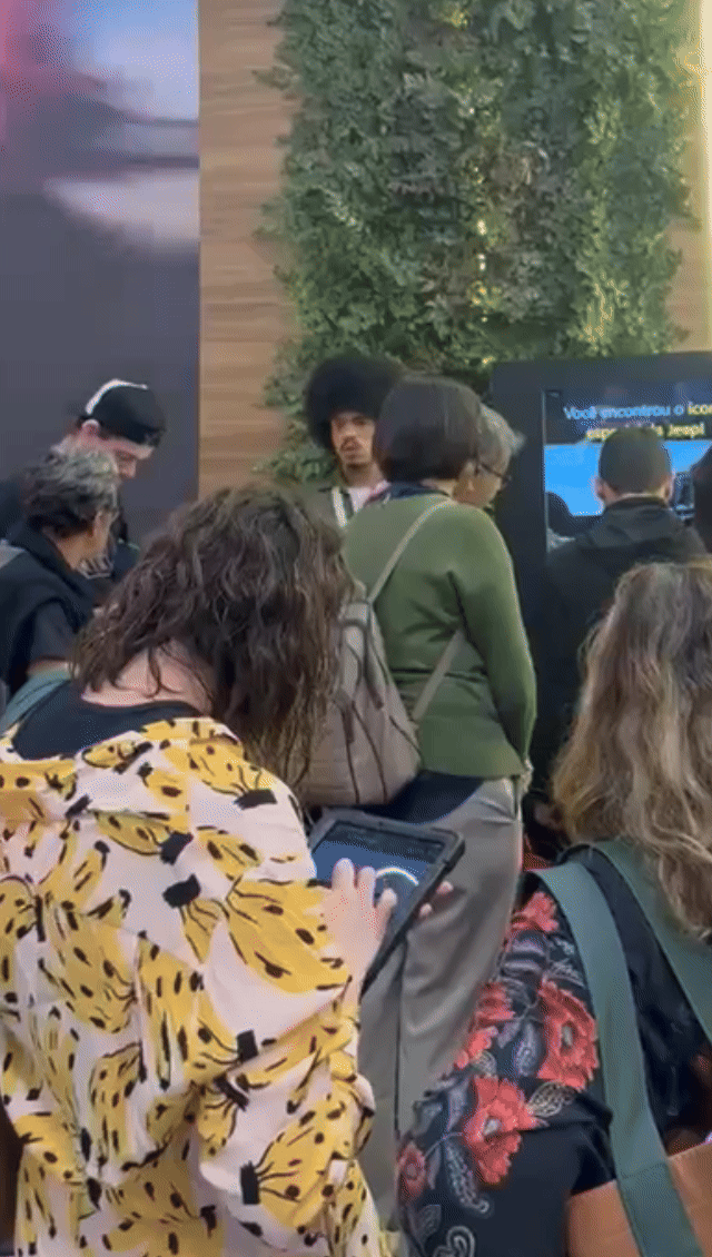 Tela vertical de 43” mostrando o game interativo “Encontre o Jeep” no Salão do Automóvel 2025. O visitante toca na tela para localizar ícones escondidos no cenário, enquanto pop-ups exibem conteúdos sobre iniciativas Jeep como Nature, Tamar e Jeep Wave.