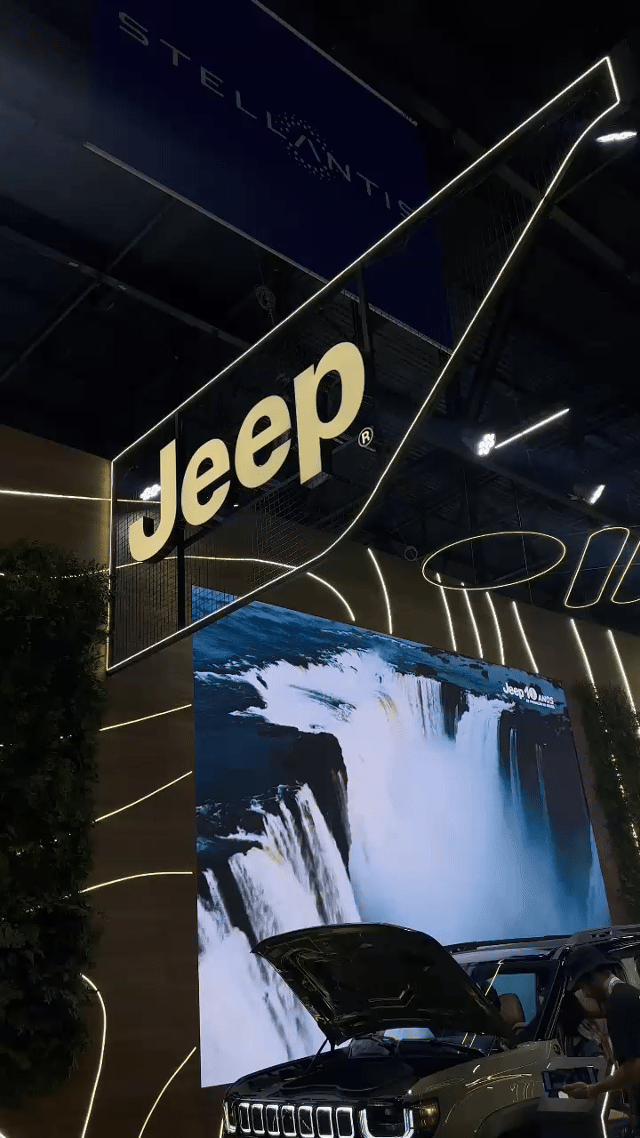 Tela vertical de 43” mostrando o game interativo “Encontre o Jeep” no Salão do Automóvel 2025. O visitante toca na tela para localizar ícones escondidos no cenário, enquanto pop-ups exibem conteúdos sobre iniciativas Jeep como Nature, Tamar e Jeep Wave.