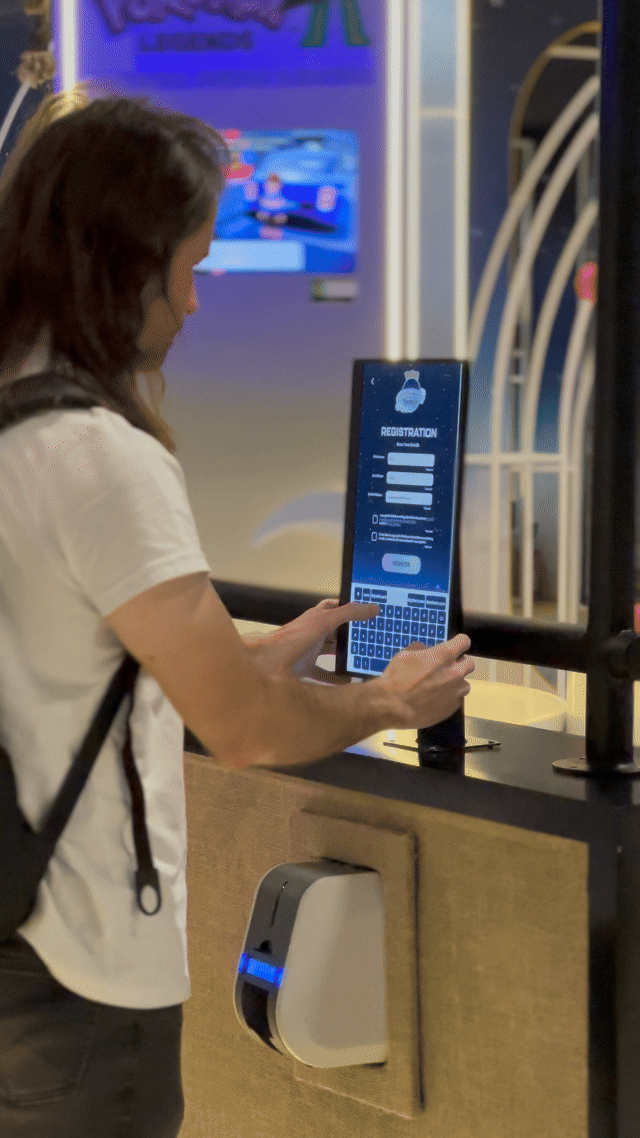 Visitantes interagem na ativação Pokémon Company | BGS 2025 – Experiência Megaevolução. Totens digitais da Phygital Solutions exibem o processo de escolha do Pokémon e da Mega Evolução, com público participando, cartões personalizados e iluminação temática do estande.
