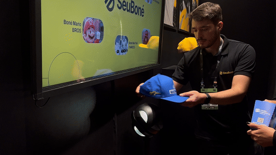 Visitantes interagem com o Museu RFID do Seu Boné na Brazil Promotion 2025, posicionando bonés históricos com tags RFID sobre suporte personalizado produzido em impressoras 3D pela Phygital Solutions, revelando histórias e curiosidades em tempo real.
