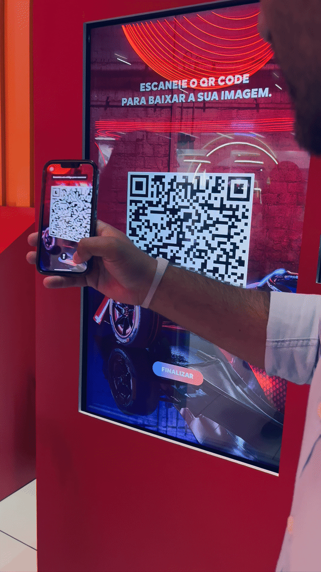 Visitante sendo fotografado em um totem da Citroën no Salão do Automóvel 2025, tendo sua imagem transformada por IA em um piloto da Fórmula E. A foto final aparece na tela ao lado, enquanto outro participante interage com a Roleta Digital personalizada com identidade da marca.