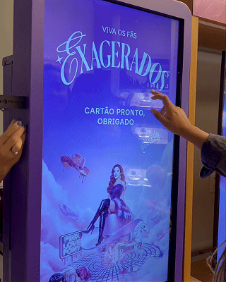 Pessoa interagindo com totem digital em loja da Vivo, realizando cadastro e tirando foto para geração de card personalizado impresso na hora durante ação pré-Lollapalooza.
