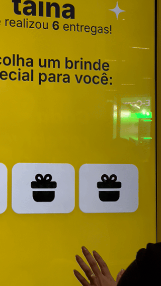 Participante joga ativação interativa da 99Entrega em um totem com joystick durante o VTEX DAY 2026, navegando em um labirinto estilo game para realizar entregas virtuais.