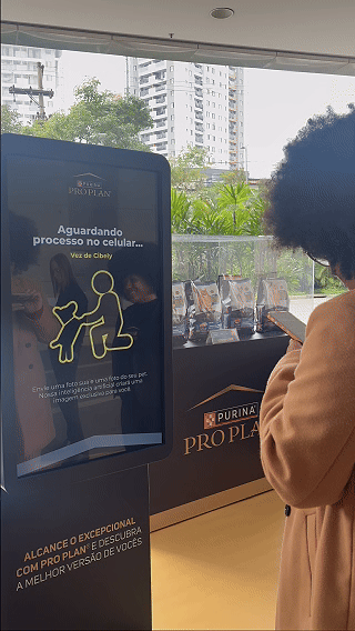 Totem interativo da ativação Nestlé Purina com QR Code para envio de fotos pelo celular. A experiência utilizava inteligência artificial para gerar uma imagem personalizada do tutor ao lado do seu pet, com resultado final direcionado para impressão.