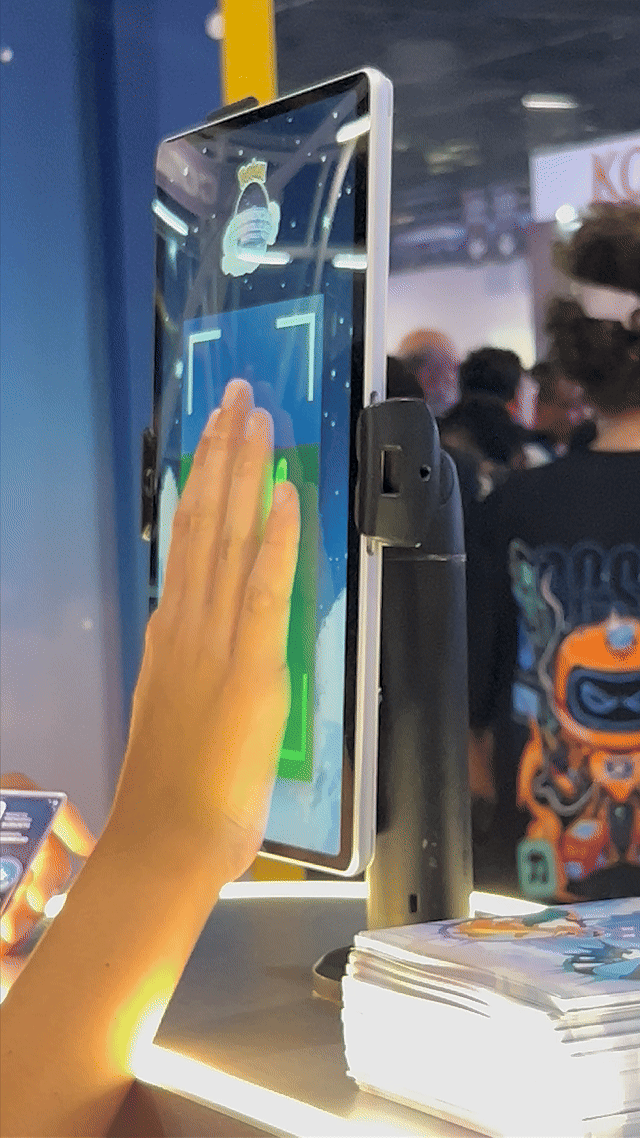 Visitantes interagem na ativação Pokémon Company | BGS 2025 – Experiência Megaevolução. Totens digitais da Phygital Solutions exibem o processo de escolha do Pokémon e da Mega Evolução, com público participando, cartões personalizados e iluminação temática do estande.