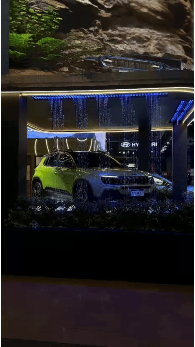 Tela vertical de 43” mostrando o game interativo “Encontre o Jeep” no Salão do Automóvel 2025. O visitante toca na tela para localizar ícones escondidos no cenário, enquanto pop-ups exibem conteúdos sobre iniciativas Jeep como Nature, Tamar e Jeep Wave.