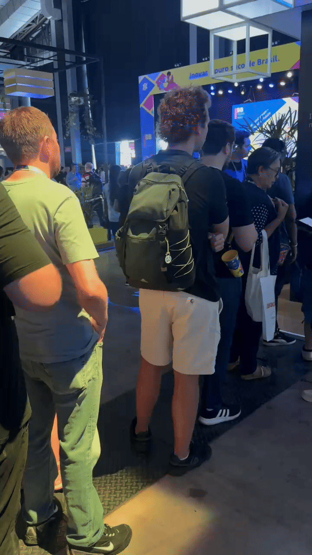 Pista de autorama personalizada da IBM com LEDs em formato de traçado, controles 3D impressos sob medida nas mãos dos participantes e estrutura técnica iluminada. Pessoas acompanham as corridas enquanto o ranking aparece em telas ao redor do estande.