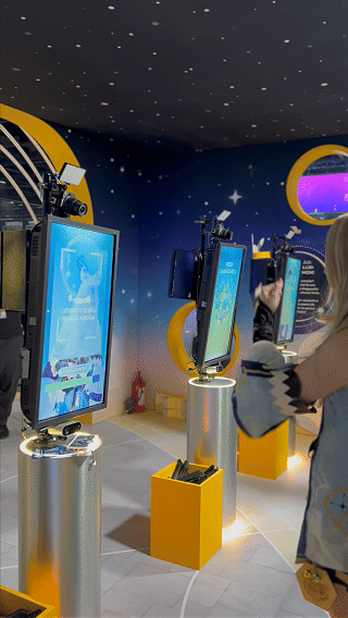 Visitantes interagem na ativação Pokémon Company | BGS 2025 – Experiência Megaevolução. Totens digitais da Phygital Solutions exibem o processo de escolha do Pokémon e da Mega Evolução, com público participando, cartões personalizados e iluminação temática do estande.