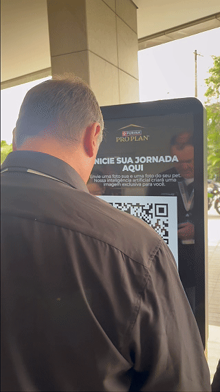 Totem interativo da ativação Nestlé Purina com QR Code para envio de fotos pelo celular. A experiência utilizava inteligência artificial para gerar uma imagem personalizada do tutor ao lado do seu pet, com resultado final direcionado para impressão.