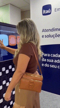 Visitante joga em totem com minigame drag and drop no estande do Itaú na AABIC 2025, interagindo com elementos visuais de forma intuitiva.