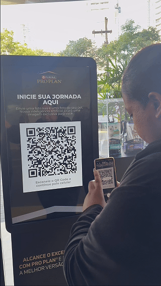 Totem interativo da ativação Nestlé Purina com QR Code para envio de fotos pelo celular. A experiência utilizava inteligência artificial para gerar uma imagem personalizada do tutor ao lado do seu pet, com resultado final direcionado para impressão.