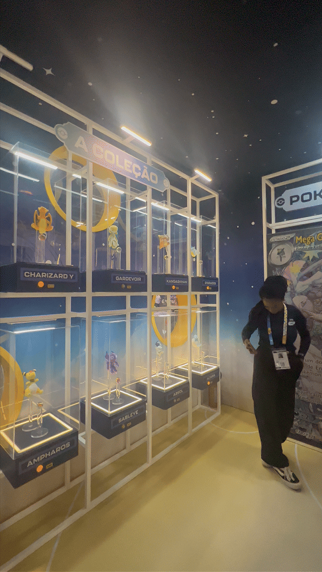 Visitantes interagem na ativação Pokémon Company | BGS 2025 – Experiência Megaevolução. Totens digitais da Phygital Solutions exibem o processo de escolha do Pokémon e da Mega Evolução, com público participando, cartões personalizados e iluminação temática do estande.