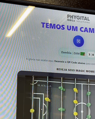 Mesa de Pebolim AI Phygital em ambiente de evento, com visual esportivo inspirado na Copa do Mundo e experiência interativa com inteligência artificial.