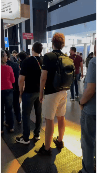 Pista de autorama personalizada da IBM com LEDs em formato de traçado, controles 3D impressos sob medida nas mãos dos participantes e estrutura técnica iluminada. Pessoas acompanham as corridas enquanto o ranking aparece em telas ao redor do estande.