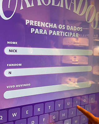Pessoa interagindo com totem digital em loja da Vivo, realizando cadastro e tirando foto para geração de card personalizado impresso na hora durante ação pré-Lollapalooza.