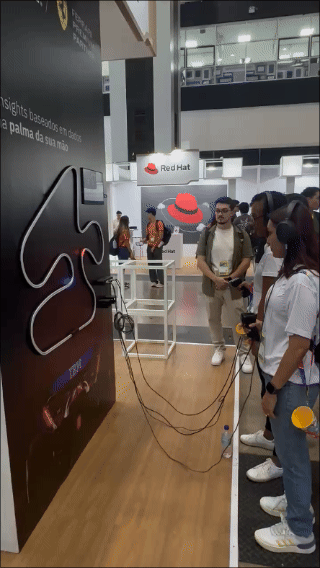 Pista de autorama personalizada da IBM com LEDs em formato de traçado, controles 3D impressos sob medida nas mãos dos participantes e estrutura técnica iluminada. Pessoas acompanham as corridas enquanto o ranking aparece em telas ao redor do estande.