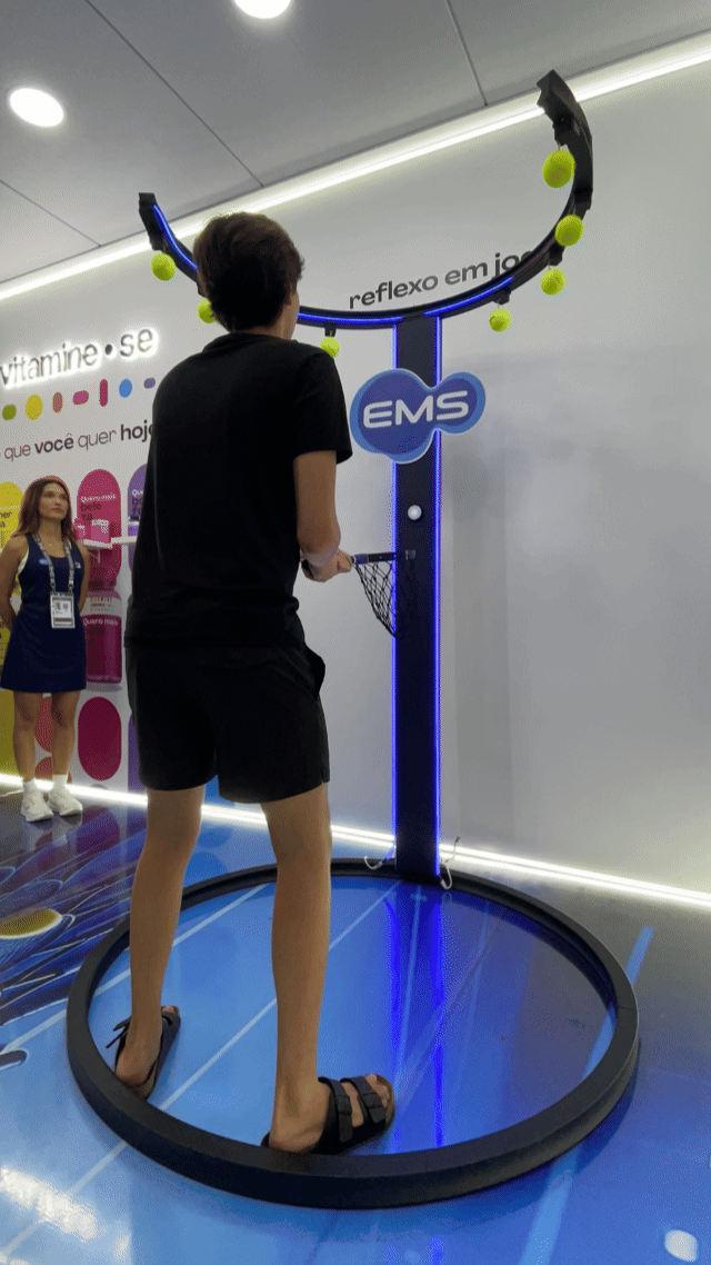 Ativação Reaction Ring no espaço da EMS durante o RIO OPEN 2026, com participante dentro da estrutura semicircular interativa enquanto o público acompanha ao redor em ambiente de evento esportivo.