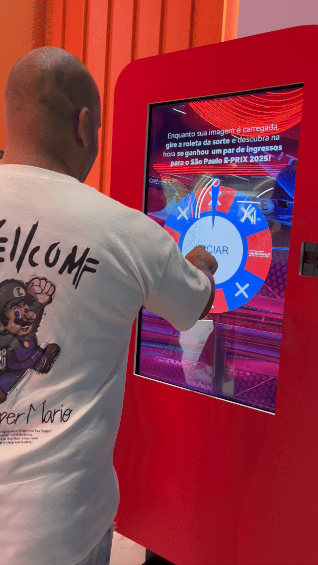 Visitante sendo fotografado em um totem da Citroën no Salão do Automóvel 2025, tendo sua imagem transformada por IA em um piloto da Fórmula E. A foto final aparece na tela ao lado, enquanto outro participante interage com a Roleta Digital personalizada com identidade da marca.