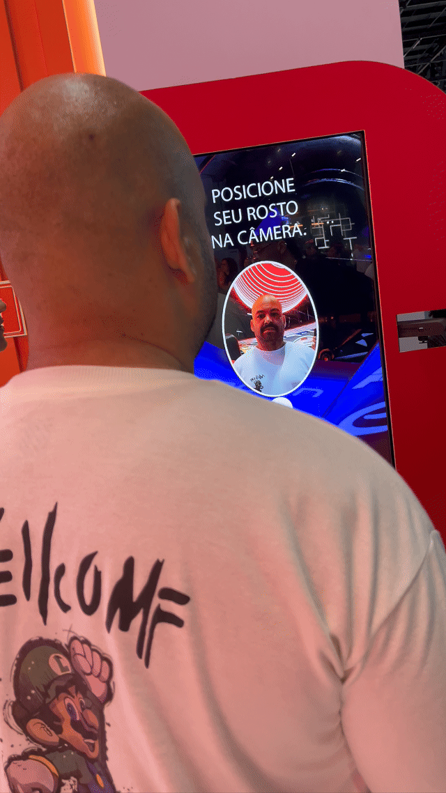 Visitante sendo fotografado em um totem da Citroën no Salão do Automóvel 2025, tendo sua imagem transformada por IA em um piloto da Fórmula E. A foto final aparece na tela ao lado, enquanto outro participante interage com a Roleta Digital personalizada com identidade da marca.