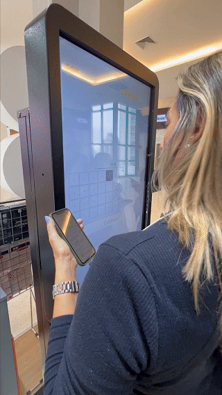 Visitante interage com totem Phygital no stand da GSK durante o TERADERM 2025, gerando avatar por IA e tendo sua imagem exibida na Social Wall em tempo real.