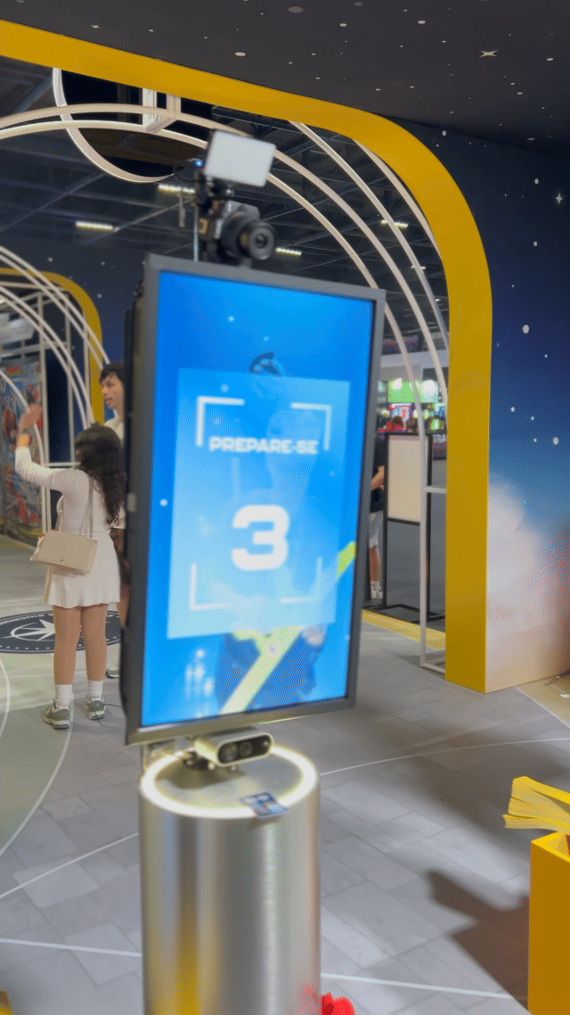 Visitantes interagem na ativação Pokémon Company | BGS 2025 – Experiência Megaevolução. Totens digitais da Phygital Solutions exibem o processo de escolha do Pokémon e da Mega Evolução, com público participando, cartões personalizados e iluminação temática do estande.