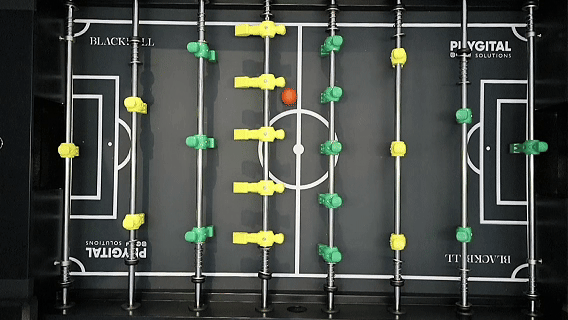 Mesa de Pebolim AI Phygital em ambiente de evento, com visual esportivo inspirado na Copa do Mundo e experiência interativa com inteligência artificial.