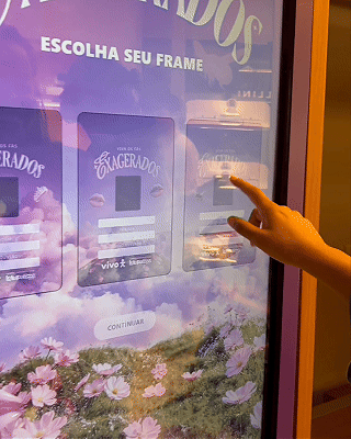 Pessoa interagindo com totem digital em loja da Vivo, realizando cadastro e tirando foto para geração de card personalizado impresso na hora durante ação pré-Lollapalooza.