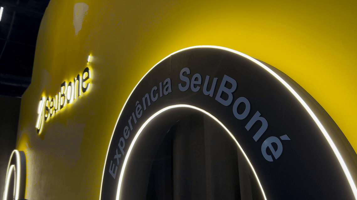 Visitantes interagem com o Museu RFID do Seu Boné na Brazil Promotion 2025, posicionando bonés históricos com tags RFID sobre suporte personalizado produzido em impressoras 3D pela Phygital Solutions, revelando histórias e curiosidades em tempo real.