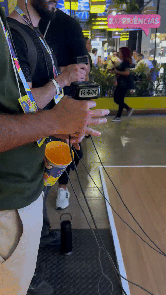 Pista de autorama personalizada da IBM com LEDs em formato de traçado, controles 3D impressos sob medida nas mãos dos participantes e estrutura técnica iluminada. Pessoas acompanham as corridas enquanto o ranking aparece em telas ao redor do estande.