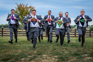 groom an groomsmen running while holding shirts open to show superhero teeshirts