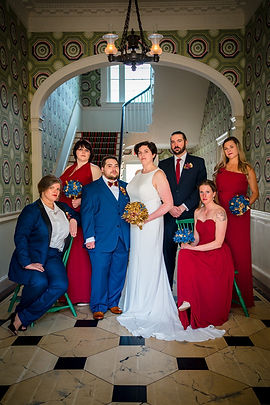 Trans and non binary wedding couple posing with wedding party in red and blue