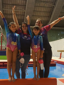 Profesoras junto a niñas celebran las medallas obtenidas en el podio de Gimnasia Artística 