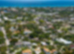 Aerial view of the coastal town of Delray Beach, FL with lush greenery, houses, and roads, leading to the blue ocean. The scene is vibrant and calm.