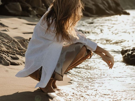 Woman enjoying gentle sunlight by the ocean, representing a balanced approach to sun exposure and sunscreen.