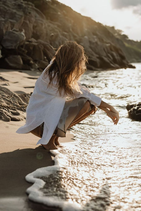 Woman enjoying gentle sunlight by the ocean, representing a balanced approach to sun exposure and sunscreen.