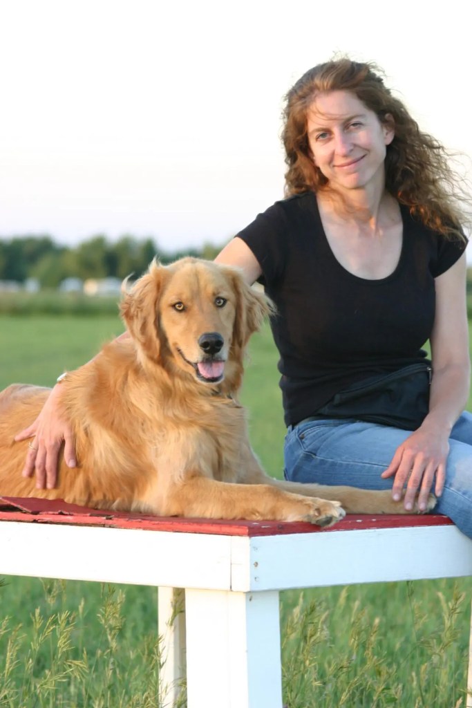 Cheryl Kolus and her dog, golden retreiver Jax, sit on a white table outside in a grassy field.