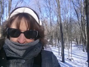 A bundled person outside during the winter taking a selfie in the woods during the day. 