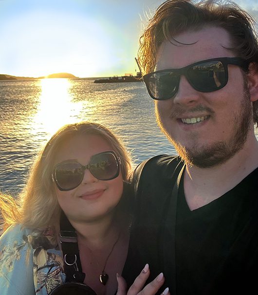 A selfie of a couple hugging overlooking a body of water at sunset.