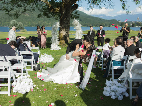 Newlyweds joyfully exit their ceremony at Sandpiper Resort, sharing a passionate kiss amidst a shower of rose petals, with guests celebrating against the stunning backdrop of lush greenery and serene waters.