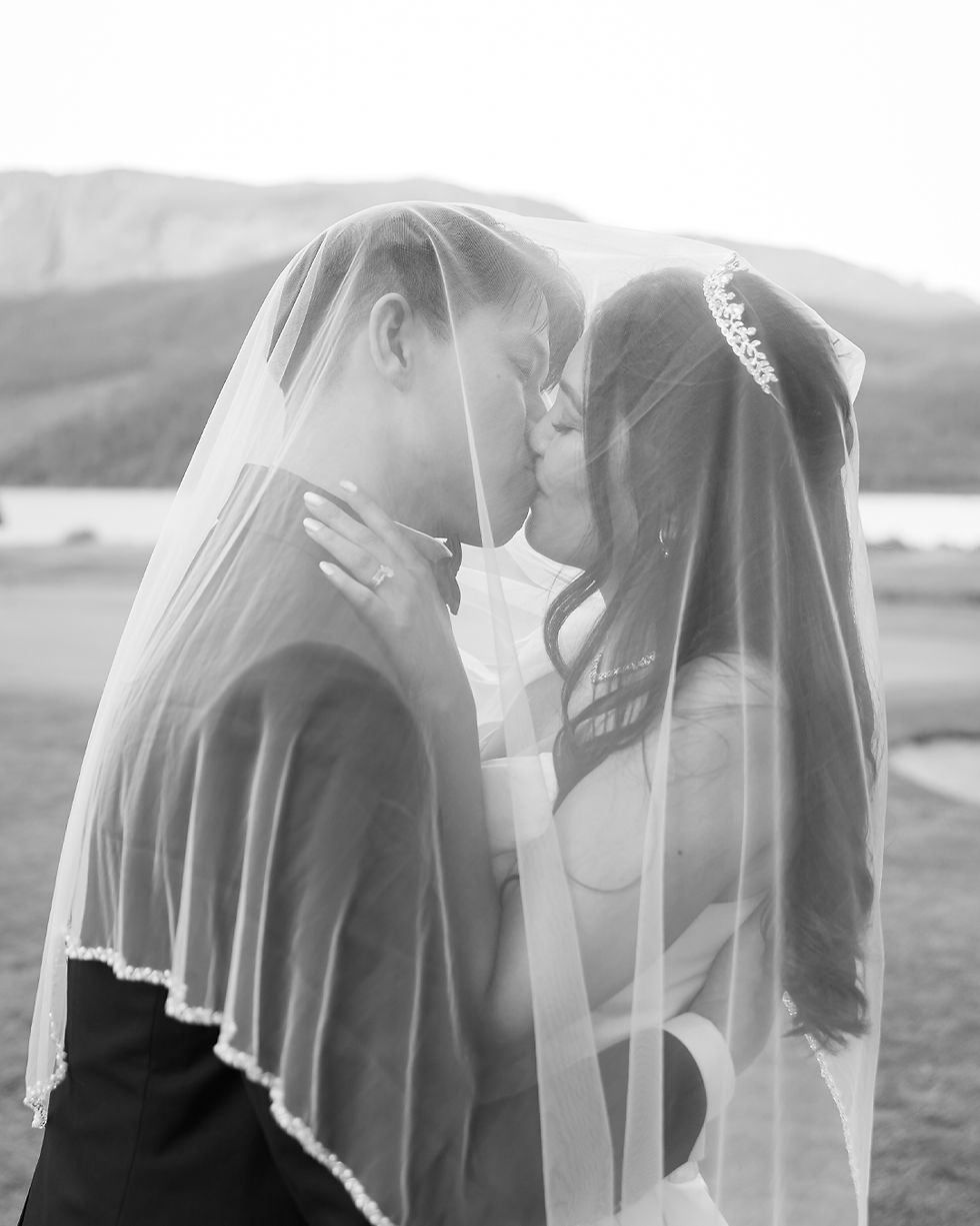 Bride and groom kissing under a veil outdoors, mountains in background. Black and white image creates a romantic, timeless mood at Sandpiper Resort wedding
