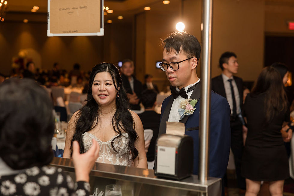 A couple in formal attire talks to a woman at a counter at a bustling event. Warm lighting and blurred guests at Terminal City Club Wedding. They are ordering icecream
