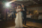 A bride and groom dance in a warmly lit restaurant. She wears a white dress, he a black tuxedo. Guests watch with joyful expressions at VanDusen Botanical Garden Wedding and Shaughnessy Restaurant wedding