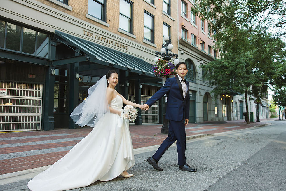 Bride and groom walk hand in hand on a city street. Bride in white gown holds bouquet; groom in dark suit. Text: The Captain French. Pre Wedding Photoshoot Vancouver – One-Stop Gastown Experience with The Eunice & Co.