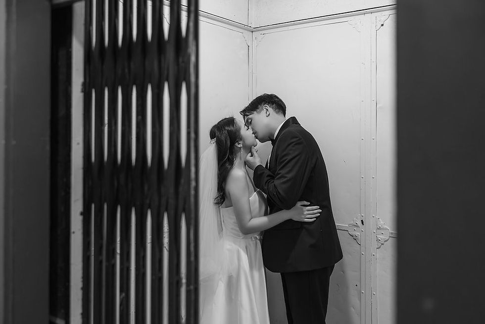 A couple in formal attire shares a kiss inside an elevator with a metal gate. The black-and-white image conveys romance and intimacy. Pre Wedding Photoshoot Vancouver – One-Stop Gastown Experience with The Eunice & Co.