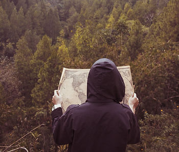 A person in a black hoodie holds up a map, looking out over a forest