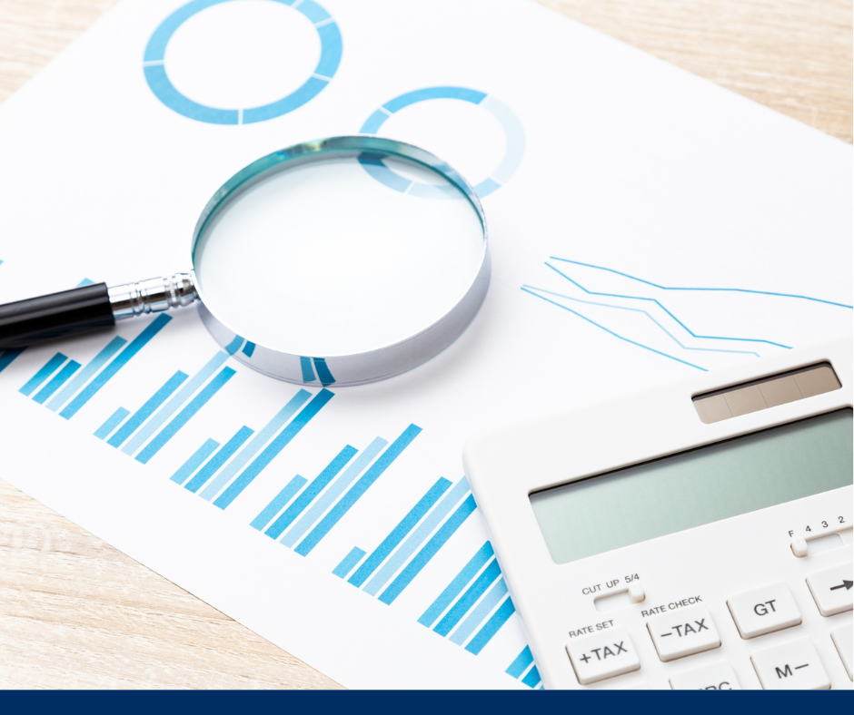 Magnifying glass on graphs with blue bars and circles, next to a white calculator on a wooden desk. Business analysis theme.